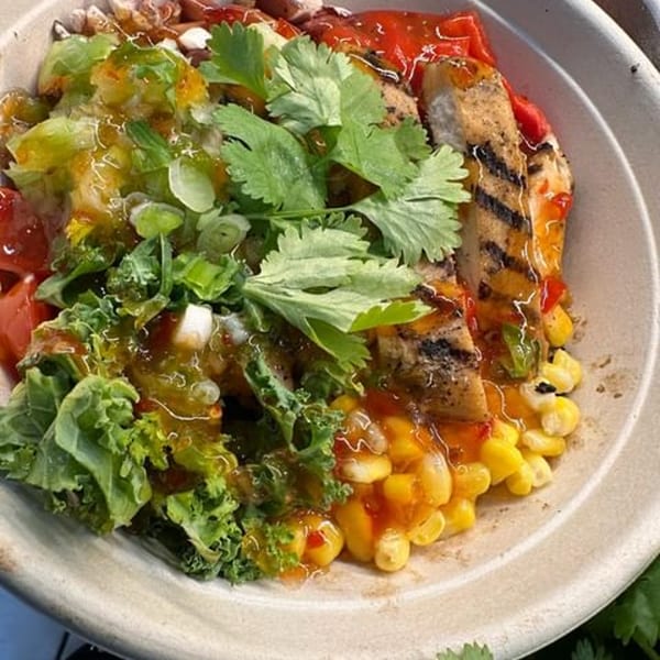 Grilled chicken, corn, red peppers, kale, and cilantro in a bowl with a sweet chili sauce.
