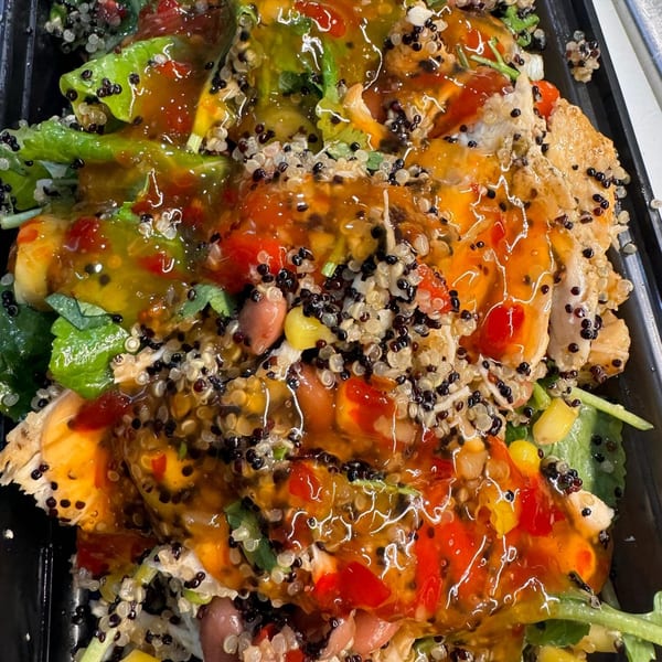 Beyond Greens and Grains' healthy chicken and quinoa salad with colorful dressing, close-up.
