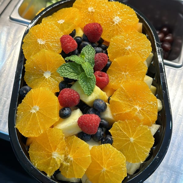 A healthy fruit salad with orange slices, raspberries, blueberries, pineapple, and mint in a black container.