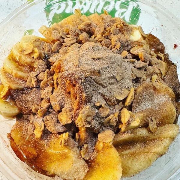 A healthy banana and granola bowl with cinnamon and syrup in a clear container.